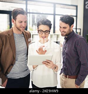 We look to one and other for guidance. a team of businesspeople discussing something on a digital tablet. Stock Photo