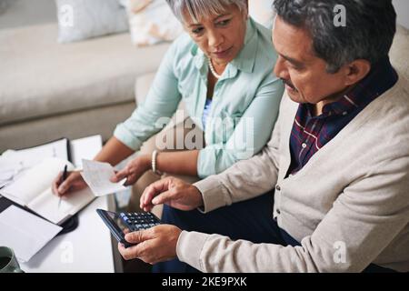 They believe in keeping track of all their expenses. an elderly couple working out a budget while sitting on the living room sofa. Stock Photo