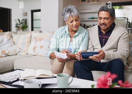 Theyve got budgeting down to an art. an elderly couple working out a budget while sitting on the living room sofa. Stock Photo