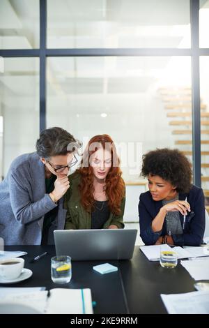 Getting everyone on the same page. three young creatives working together on a laptop in a modern office. Stock Photo