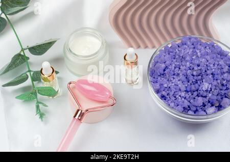 Rose quartz facial roller with face oil, face moisturizer and lavender sea salt on a white table background. Facial massage kit for lifting massage th Stock Photo