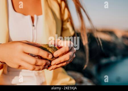 Woman's hands opening a fig to eat. Fresh ripe fig fruit in the hands. A young woman eats figs on the beach, near sea. Ficus carica, Fig - green Stock Photo