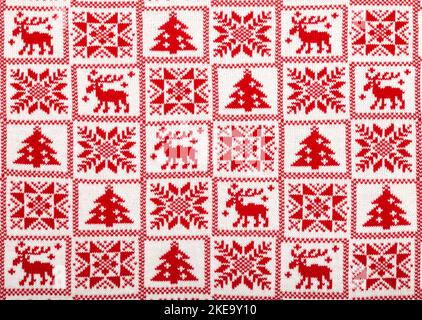 Red knitted fabric with white moose, fir tree and snowflake Scandinavian style geometric ornament cristmas background Stock Photo