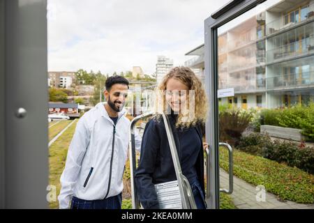 Young technicians entering building with ladder Stock Photo