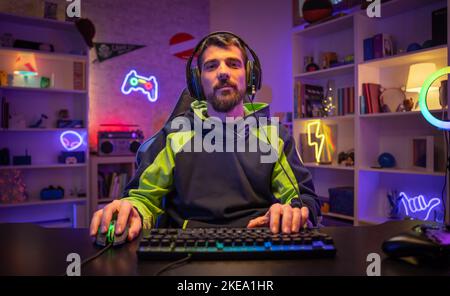 Happy gamer portrait playing games on the computer looking at camera while streaming gaming room. Stock Photo