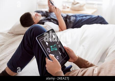 Brothers lying on bed and using phone and tablet Stock Photo