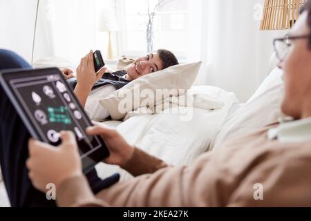 Brothers lying on bed and using phone and tablet Stock Photo