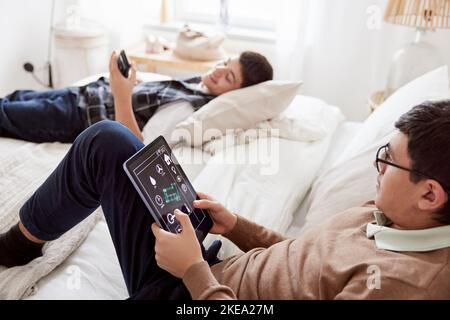 Brothers lying on bed and using phone and tablet Stock Photo