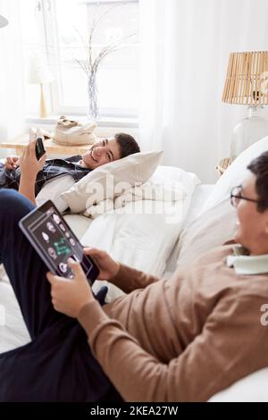 Brothers lying on bed and using phone and tablet Stock Photo