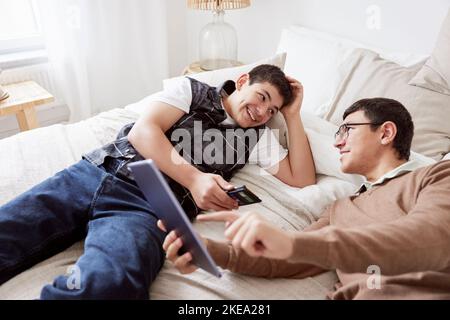 Brothers lying on bed and using phone and tablet Stock Photo