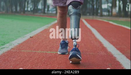 Back view of a disabled athlete man with prosthetic leg walking on running track Stock Photo
