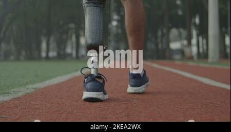 Back view of a disabled athlete man with prosthetic leg walking on running track Stock Photo