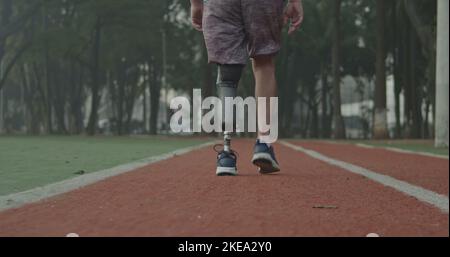 Back view of a disabled athlete man with prosthetic leg walking on running track Stock Photo