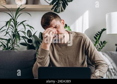 Close up of unhappy young man working on laptop massage eyes suffer from blurred vision or dizziness, exhausted caucasian male feel unwell having head Stock Photo