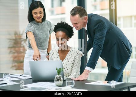 Show him that one. three businesspeople gathered around a laptop in the office. Stock Photo