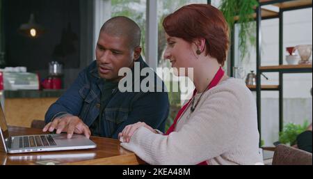 Diverse male manager explains online orders to female staff. Two employees in front of computer laptop screen talking about small business protocol Stock Photo