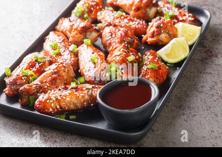 Baked Hoisin Sauce Chicken Wings with sesame served with green onion, lime close-up in a plate on the table. Horizontal Stock Photo
