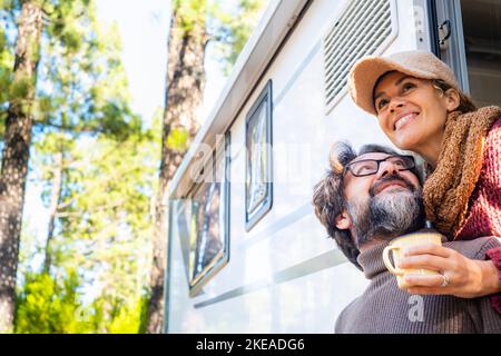 Happy couple enjoying outdoor forest destination smiling together outside their camper van vehicle. Concept of alternative travel vacation and free of Stock Photo
