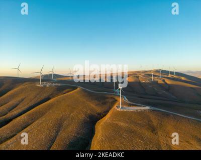 Aerial view of multiple wind turbines standing on a hill and generating electricity at sunrise Stock Photo