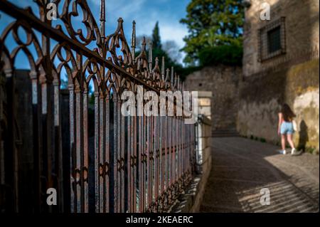 Young girl walking on a desert street with old rusty fence and long shadows on the street with blue sky Stock Photo