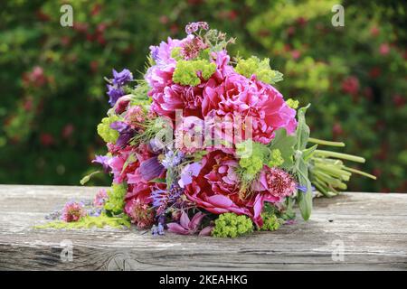 Colourful bouquet, red, pink and purple with peonies and columbines lying on a wooden garden bench Stock Photo