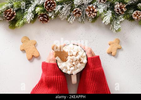 Top view of Christmas hot chocolate cup coffee with marshmallow, Gingerbread man cookies in female hands on white background. Festive food for Xmas ho Stock Photo