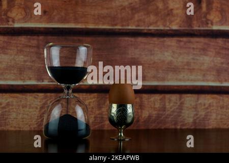 Hourglass with egg in egg cup on a polished wooden shelf Stock Photo