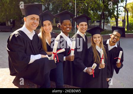 Young joyful people graduate university dressed in black gown standing on street Stock Photo