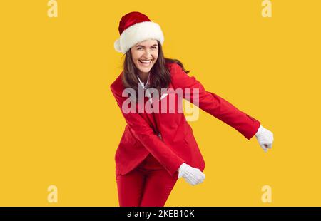 Laughing cheerful woman wearing Santa style dancing swish backpack dance on yellow background. Stock Photo