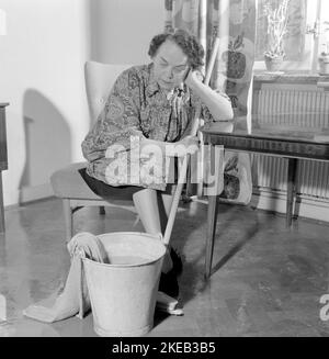Cleaning the floor back then. A woman looks very tired and worn out when sitting on a chair, having a rest in the work of cleaning the floors. Sweden 1956 Conard ref 3160 Stock Photo