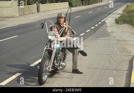 In the 1960s. A young man on his Harley Davidson motorcycle. The law of wearing a safety helmet is not yet in force and at this time it was popular to wear leather caps. Sweden 1968 CV72 Stock Photo