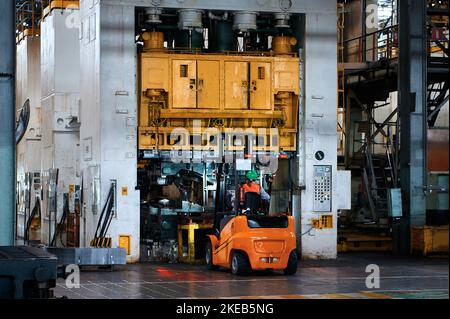 Giant stamping press. Sheet metal stamping. Electric forklift brings a pack of metal to work the press. Stock Photo