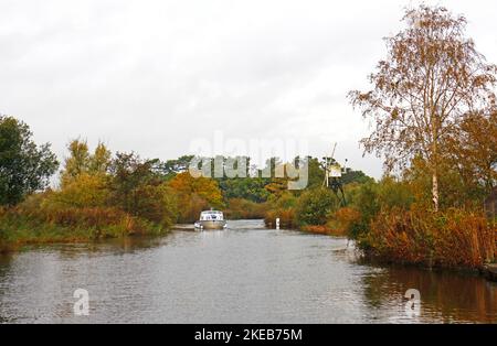 A view of a cruiser on the River Ant on the Norfolk Broads passing by Boardmans Mill in autumn by How Hill, Ludham, Norfolk, England, United Kingdom. Stock Photo