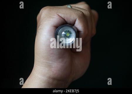 An LED flashlight held in a person's hand on a black background. Close up view. Stock Photo