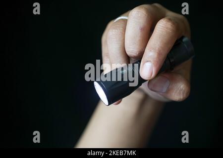 Close-up of a person's hand holding a flashlight on a black background. Close up view. Stock Photo