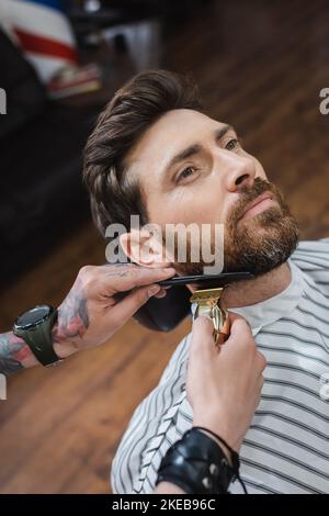 high angle view of brunette man near barber trimming his beard with hair clipper,stock image Stock Photo