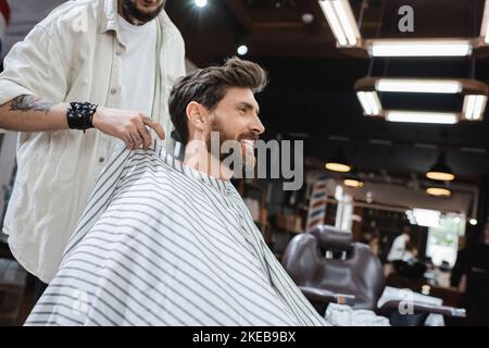 hairstylist putting hairdressing cape on happy client in barbershop,stock image Stock Photo
