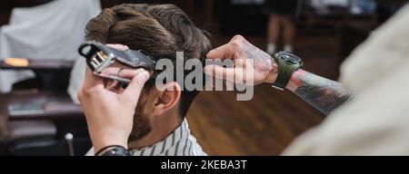 Tattooed barber combing and trimming hair of man in barbershop, banner,stock image Stock Photo
