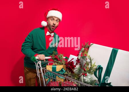 Photo of impressed funny guy dressed xmas green cardigan buying noel gifts shoppers isolated red color background Stock Photo