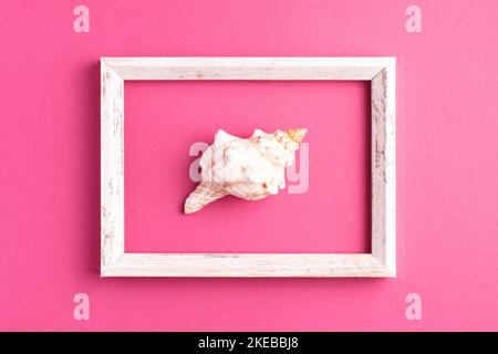 Minimalistic flat lay composition with vintage picture frame and seashell on bright pink background. Top view, summer time concept. Stock Photo
