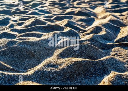 Undulating shapes of sand in sunset light on beach. Stock Photo