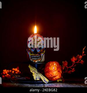 A characteristic calavera, which in Mexican tradition celebrates the day of the dead, with a lit candle next to it Stock Photo