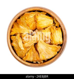 Dehydrated pineapple pieces, in a wooden bowl. Chunks of dried fruits of Ananas comosus, used as snack, for muesli or trail mixes. Stock Photo