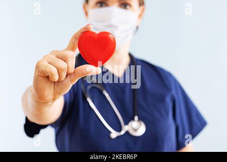 Female doctor with stethoscope holding red heart on blue background Stock Photo