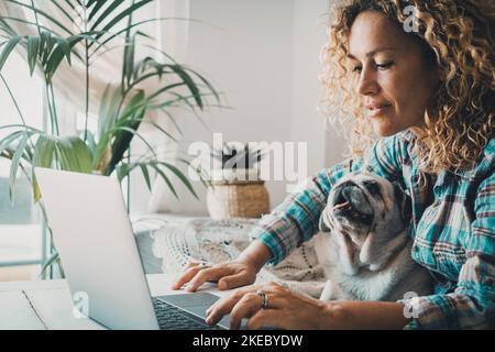Smart working at home with female and her puppy working on computer together in friendship and love. Cheerful happy woman write on laptop with a dog on her legs. Concept of domestic animals lifestyle Stock Photo