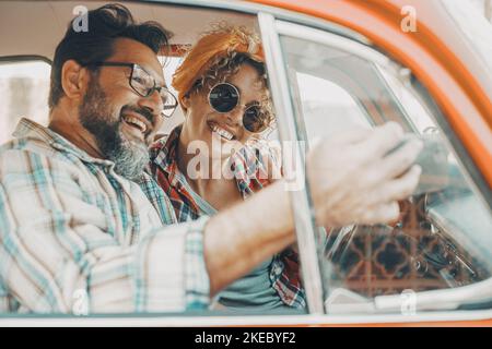 Happy couple having fun inside a car during travel adventure. Cheerful man and woman smiling and laughing a lot together. People enjoying vehicle trip in friendship and relationship. Concept of drive Stock Photo