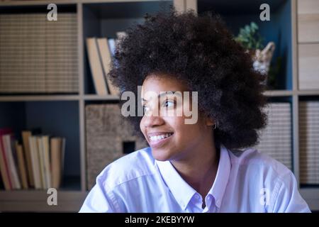 Attractive dark skinned young woman with curly Afro hairstyle looking out through window. Thoughtful african american businesswoman smiling and looking away at office. Female lady dreaming about future Stock Photo