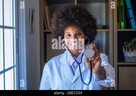 Portrait of happy smiling female african american doctor in uniform showing stethoscope for checking heartbeat rate. Healthcare worker showing examination tool medical equipment to camera Stock Photo