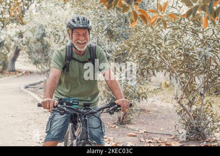 One old mature man riding a bike and enjoying nature outdoors having fun. Senior having a healthy and fit lifestyle. Stock Photo