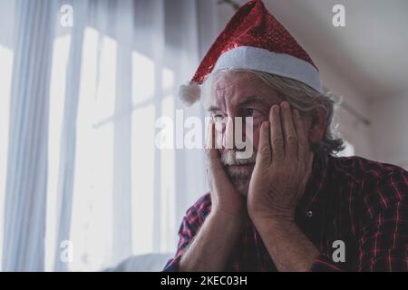 Portrait of one old and mature man sitting on the sofa of his home celebrating the Christmas Day alone and lonely and isolated from his family for the coronavirus Stock Photo